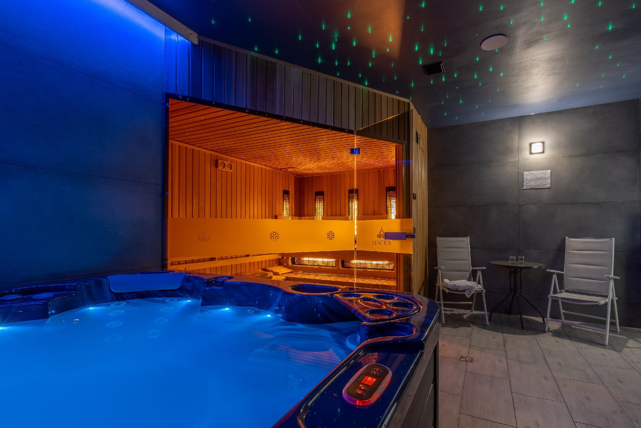 Nowoczesne wnętrze strefy relaksu z podświetlanym jacuzzi, sauną fińską z przeszklonym frontem i przestrzenią wypoczynkową z dwoma krzesłami i stolikiem, oświetlenie punktowe imitujące gwiazdy...