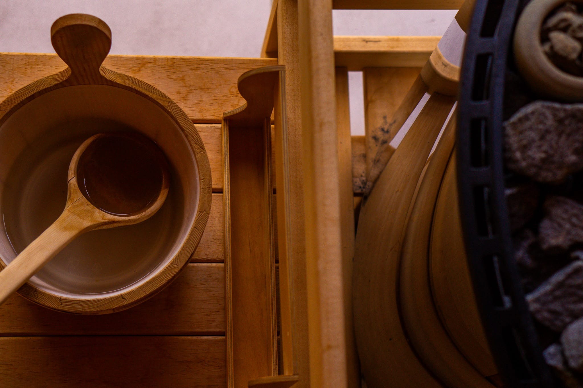 Drewniane akcesoria w saunie: ceber z wodą i chochla oraz piec z kamieniami, ujęcie z góry.