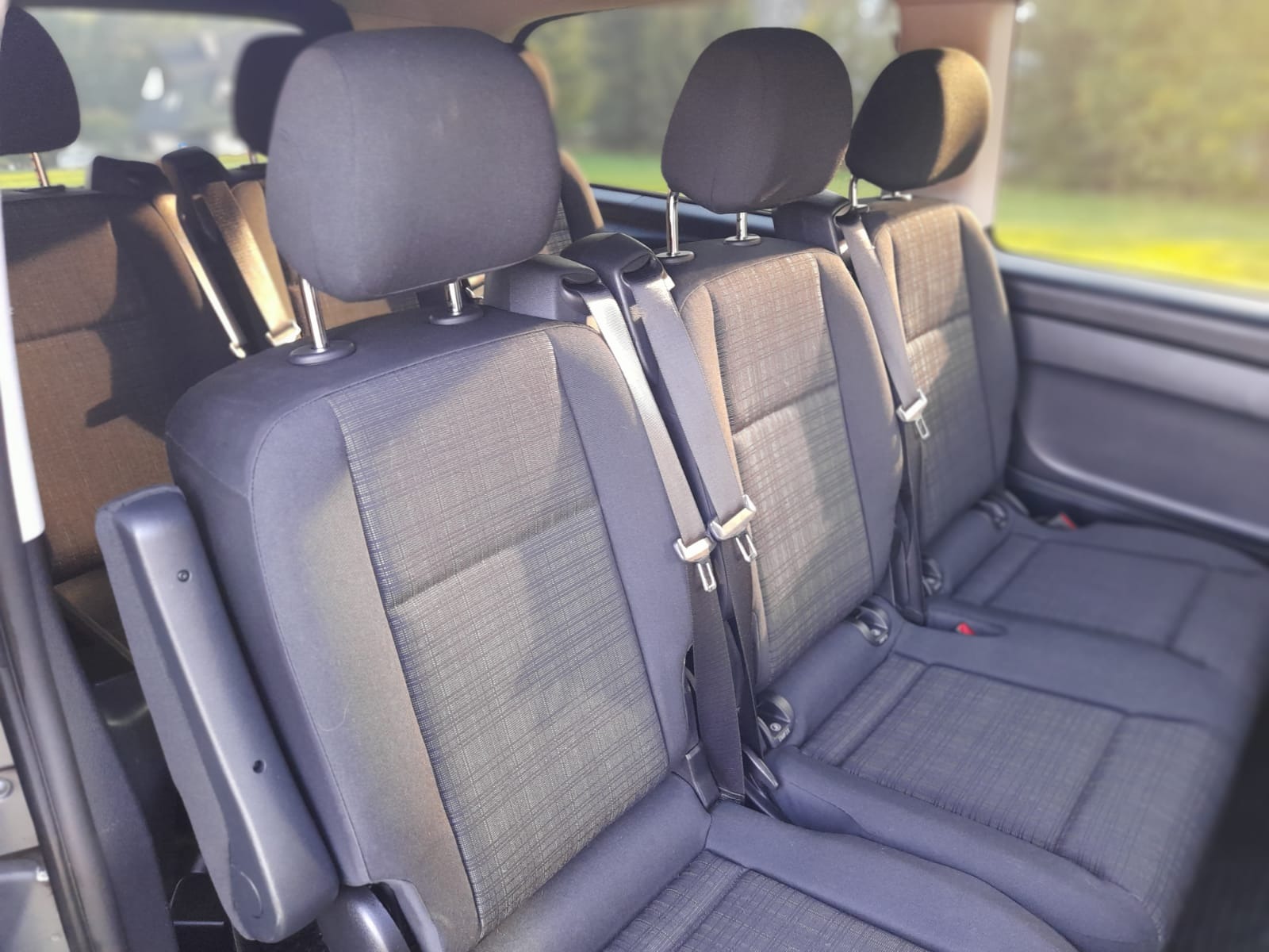 Wnętrze busa z trzema rzędami foteli z tapicerką w odcieniach szarości i pasami bezpieczeństwa, widok z perspektywy pasażera.
