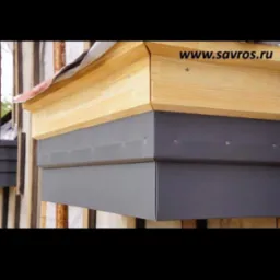 Fragment dachu z widocznymi obróbkami blacharskimi w kolorze szarym, drewnianą konstrukcją i fragmentem pokrycia dachowego, widoczne łączenia blachy za pomocą nitów.