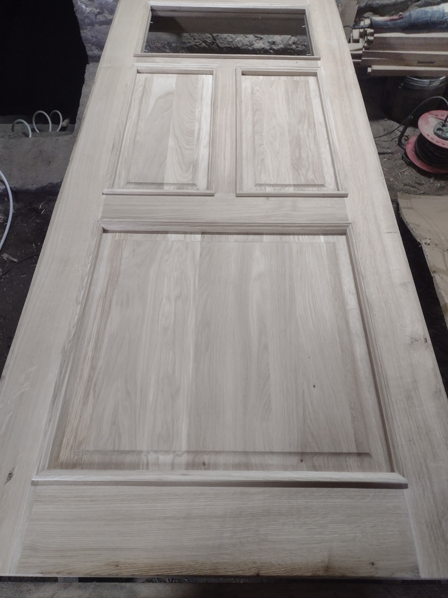 Surowa, drewniana konstrukcja dachu z widocznymi elementami ramy i wypełnieniami, ułożona na płasko w warsztacie, z kablem elektrycznym w tle.