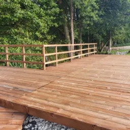 Drewniany taras z barierką w otoczeniu zieleni, widok na ogród i drzewa.