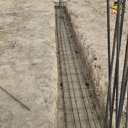 MAX-ECO - Zbrojenie fundamentów w wykopie, widok z góry. W tle betoniarka i ciężarówka. Etap budowy domu jednorodzinnego.