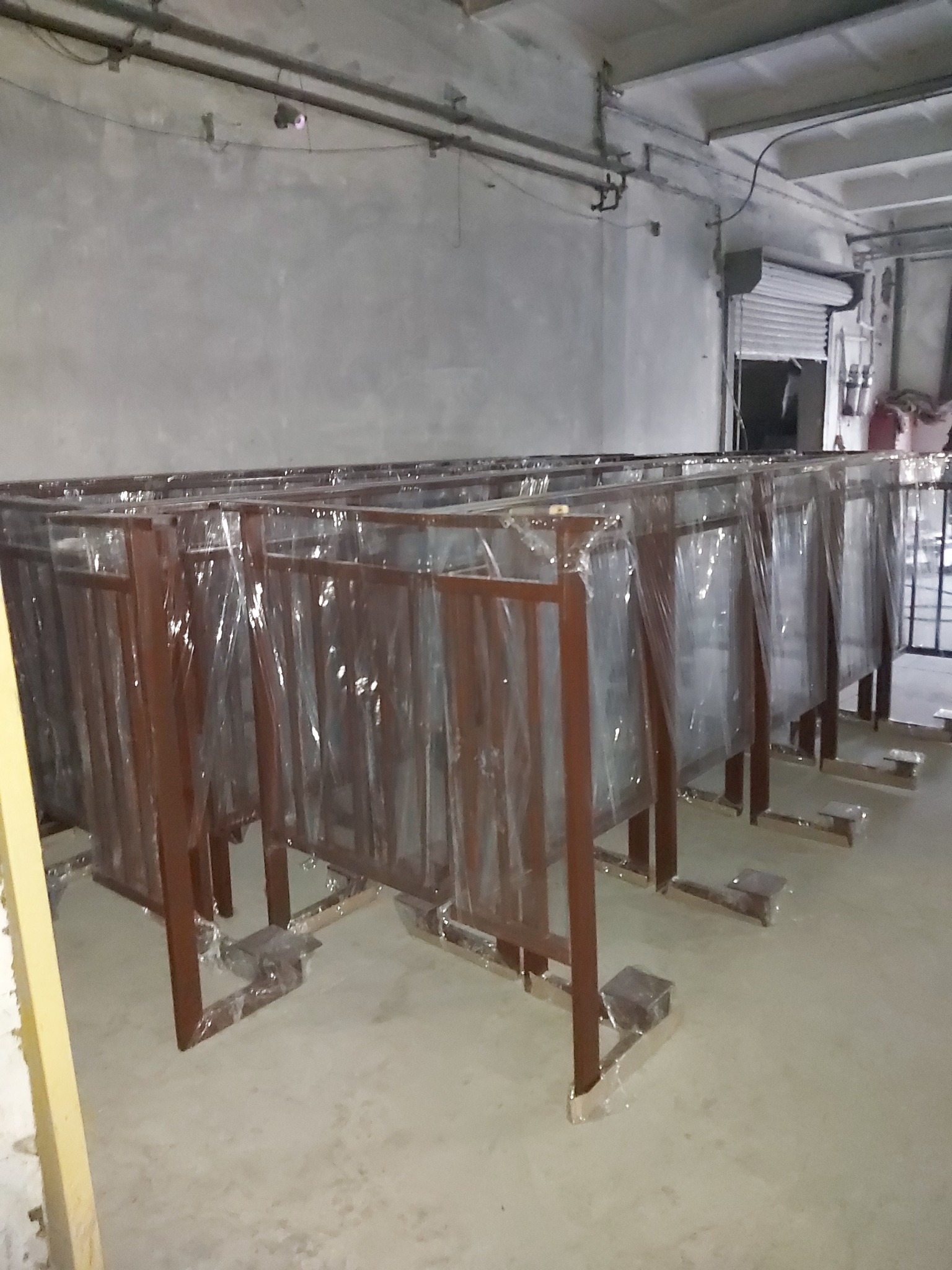 Rzędy metalowych konstrukcji, prawdopodobnie balustrad balkonowych, po obróbce i zabezpieczone folią, stoją w hali produkcyjnej, gotowe do transportu.