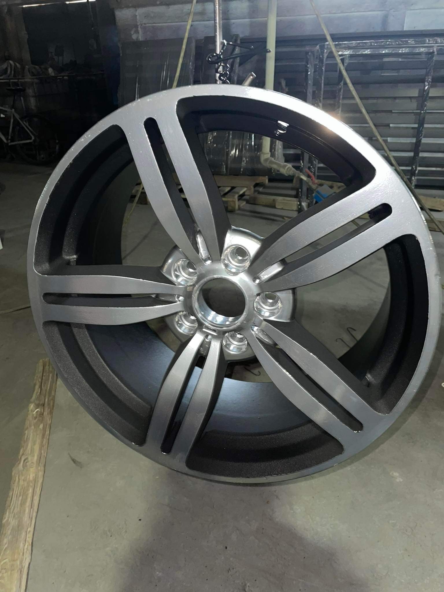 Szara felga samochodowa zawieszona na haku w warsztacie, po obróbce, z widocznymi śladami świeżego lakieru