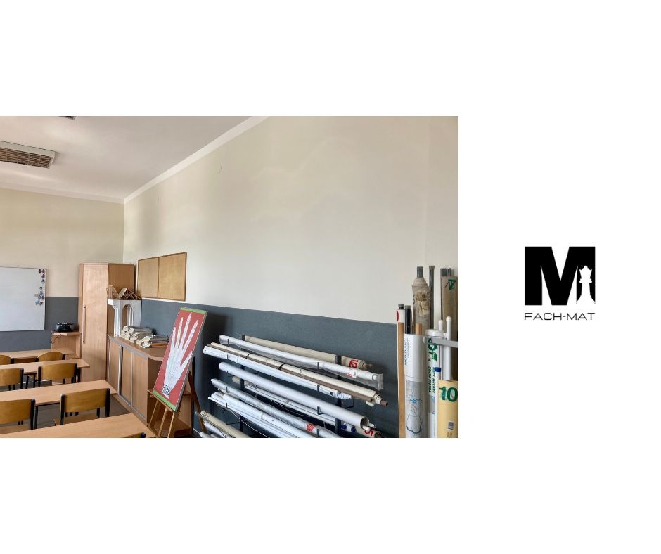 Wyremontowana sala lekcyjna z gładkimi, pomalowanymi ścianami w odcieniach beżu i szarości, widoczne biurka, szafki, tablica oraz zwinięte plansze i logo firmy Fach-Mat po prawej stronie.