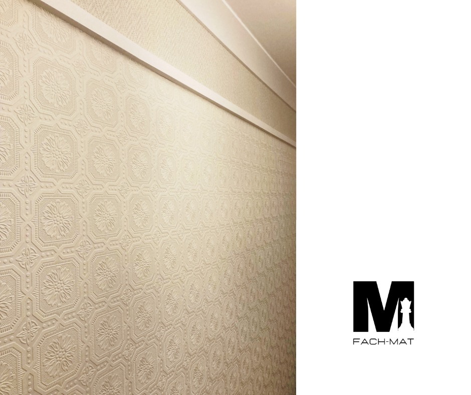 Ściana pokryta beżową, tłoczoną tapetą z motywem kwiatowym i geometrycznym, wykończona białą listwą przysufitową; po prawej stronie widoczne logo firmy Fach-Mat.