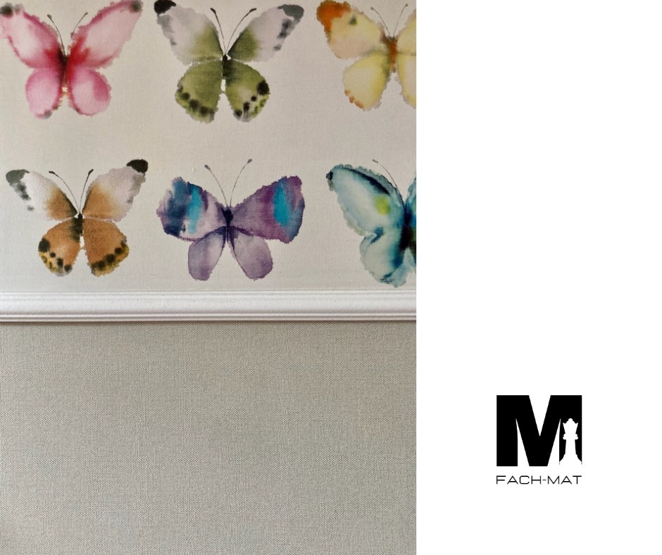 Ściana z tapetą w motyle akwarelowe, oddzielona białym dekoracyjnym pasem od dolnej części ściany pokrytej jednolitą tapetą w odcieniach szarości, z widocznym logo firmy w prawym dolnym rogu.