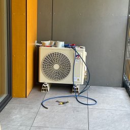 Energomax Sp. z o.o. - Zewnętrzna jednostka klimatyzacji marki Gree, zamontowana na balkonie na specjalnych wspornikach, z podłączonymi przewodami i narzędziami serwisowymi na górze, widoczne płytki podłogowe i fragment...