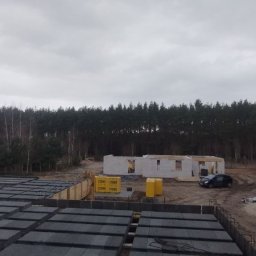 OlegDyshko - Budowa domu murowanego w stanie surowym otwartym z widocznym stropem Teriva, bloczkami Ytong i lasem w tle, pochmurny dzień.