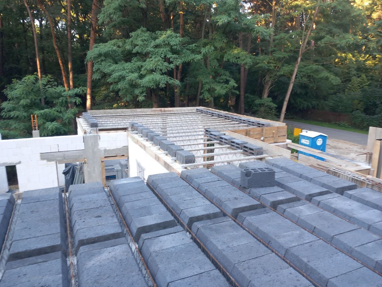 Wieniec stropowy z szalunkami traconymi na budowie domu jednorodzinnego, widok z góry na otoczenie leśne i drogę.