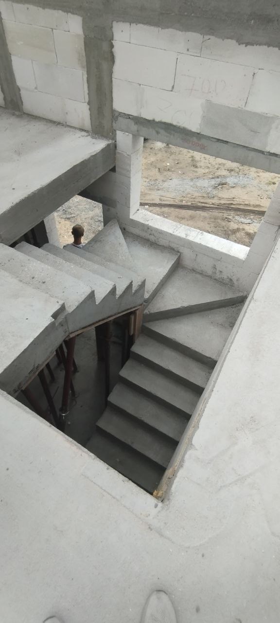 Surowe, betonowe schody w trakcie budowy domu murowanego, widoczne białe bloczki i podpory schodów, w tle sylwetka osoby.