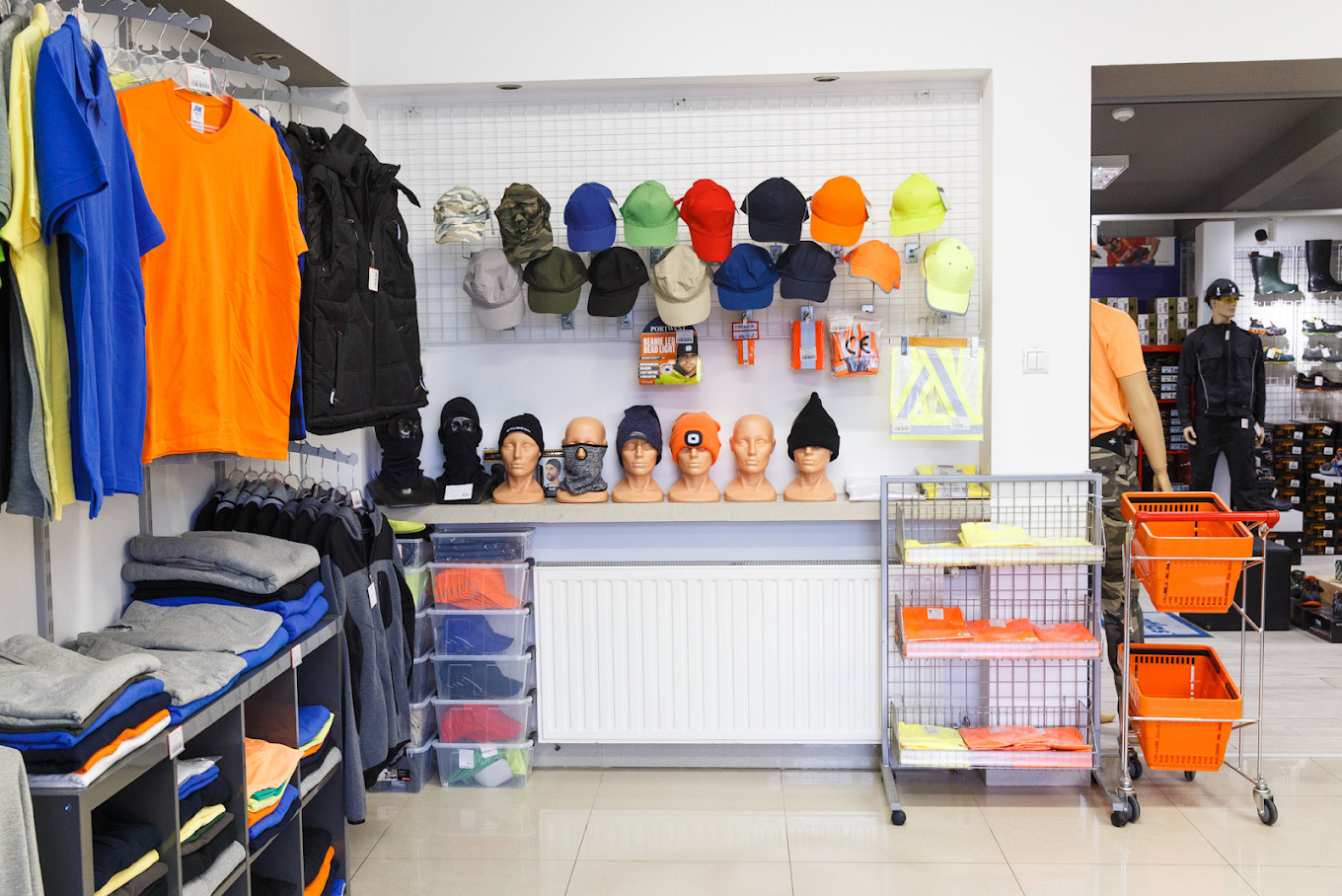 Wnętrze sklepu z odzieżą roboczą: ekspozycja koszulek, kamizelek, czapek i kominiarek na manekinach i w koszykach.