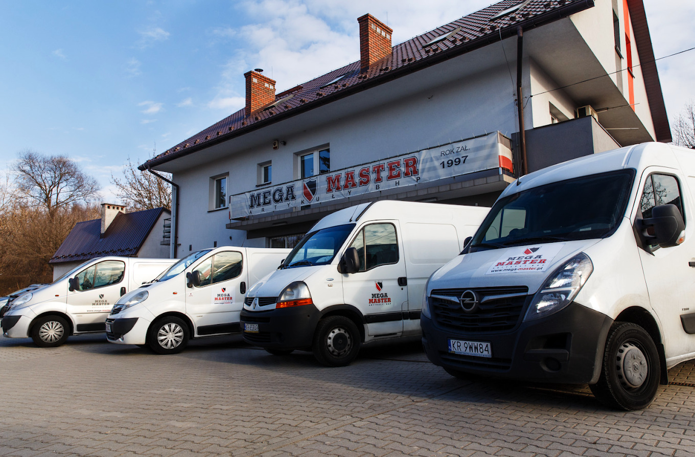 Flota białych samochodów dostawczych z logo firmy Mega Master zaparkowana przed budynkiem firmy z szyldem informującym o roku założenia 1997.