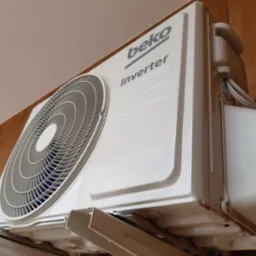 Biała jednostka wewnętrzna klimatyzacji Beko Inverter zamontowana na drewnianej ścianie, widok z dołu, widoczne przewody.