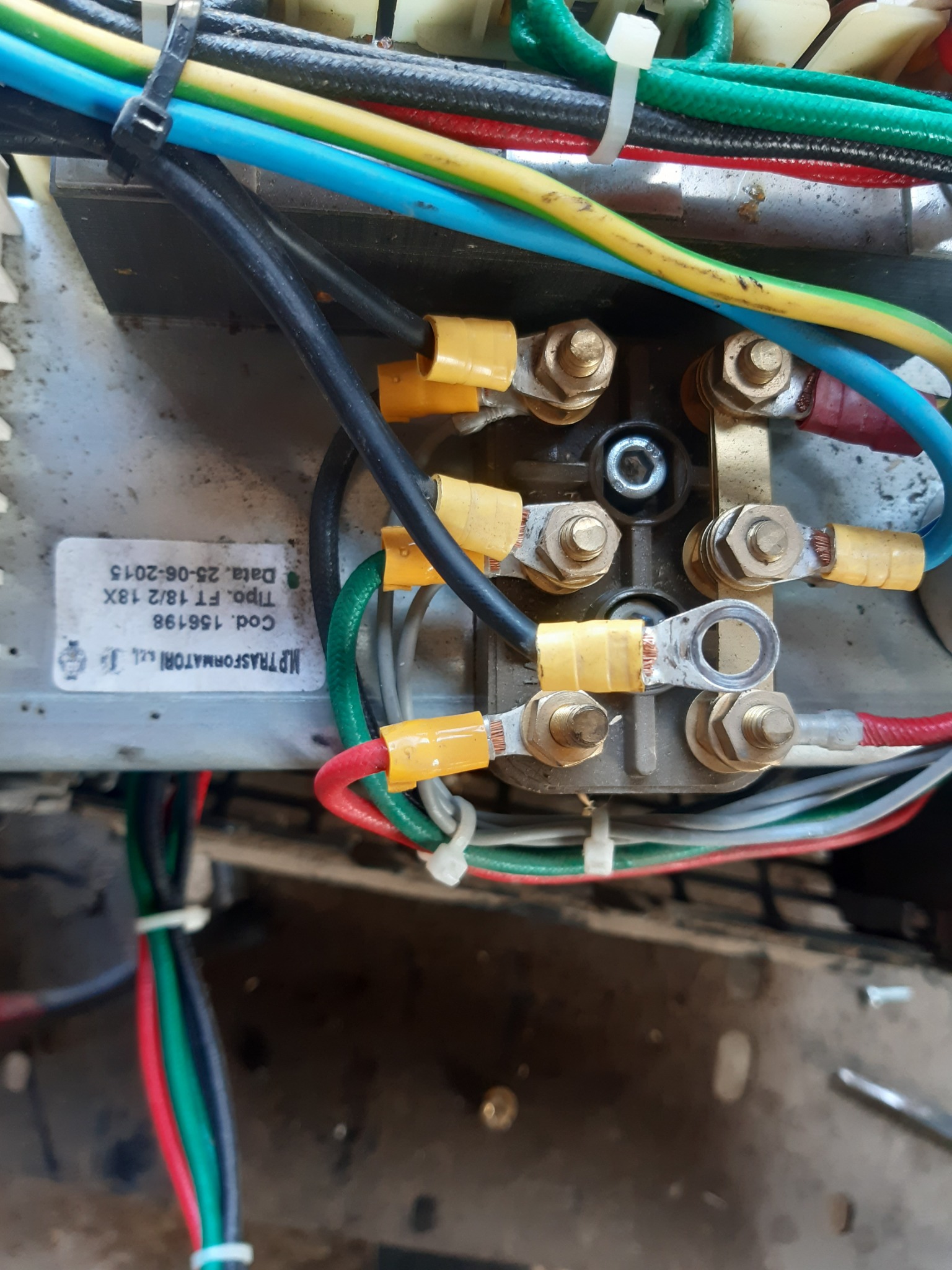 Szczegółowe ujęcie połączeń elektrycznych w urządzeniu, widoczne przewody w różnych kolorach (czarny, zielony, czerwony, niebieski, żółty) z końcówkami w izolacji, przykręcone do metalowej listwy...