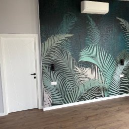 DADAEVS SPÓŁKA Z OGRANICZONĄ ODPOWIEDZIALNOŚCIĄ - Pokój po remoncie z tapetą w motywy tropikalne, białe drzwi z czarną klamką i klimatyzator na ścianie.