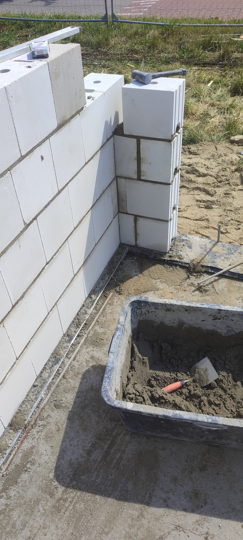 Wznoszenie ściany z bloczków białych w Piastowie, widoczna zaprawa w pojemniku i poziomica na górze ściany.