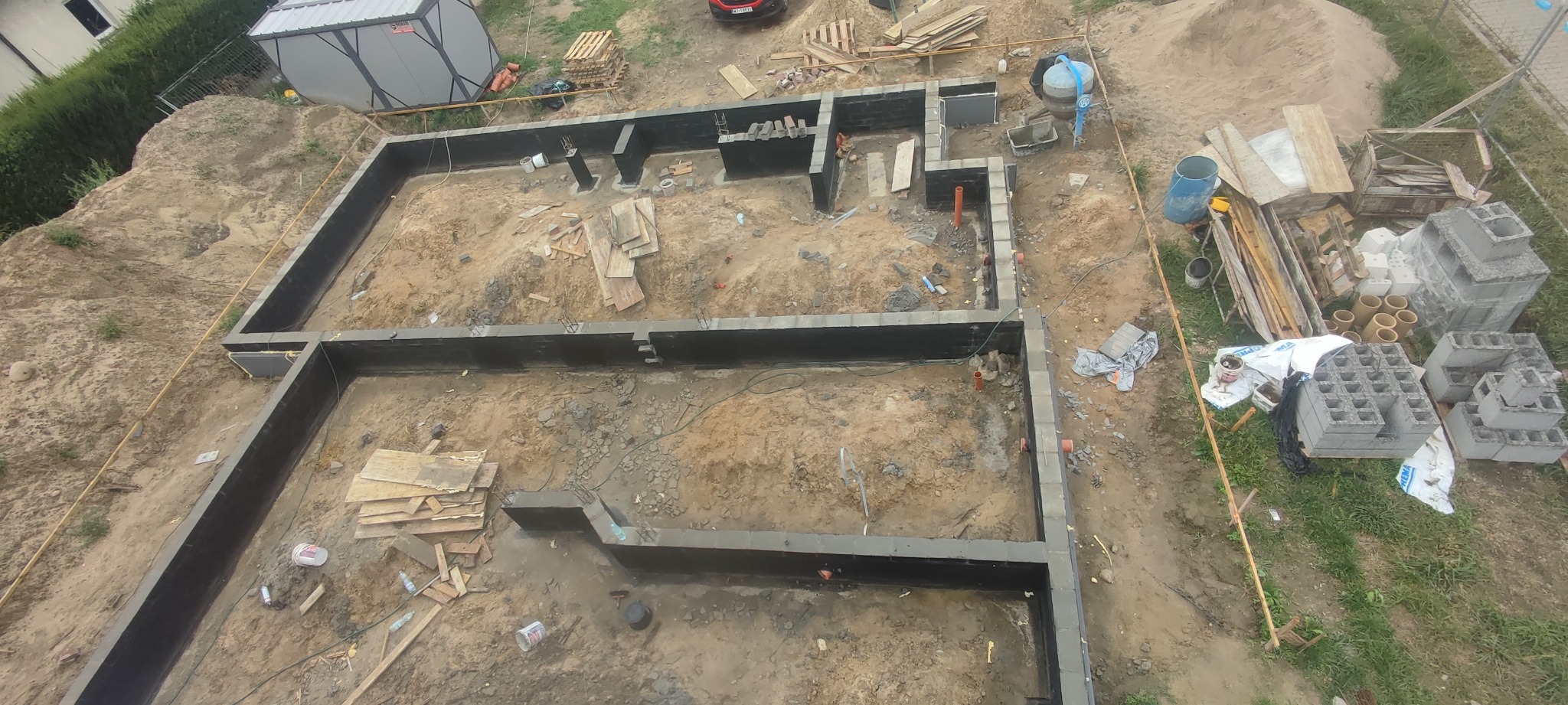 Zalane fundamenty domu jednorodzinnego z hydroizolacją, widok z góry, z przygotowanymi pionami kanalizacyjnymi i elementami szalunków.