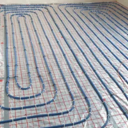 Niebieskie rury ogrzewania podłogowego zamocowane do folii z siatką w nowym budynku, widok z góry.