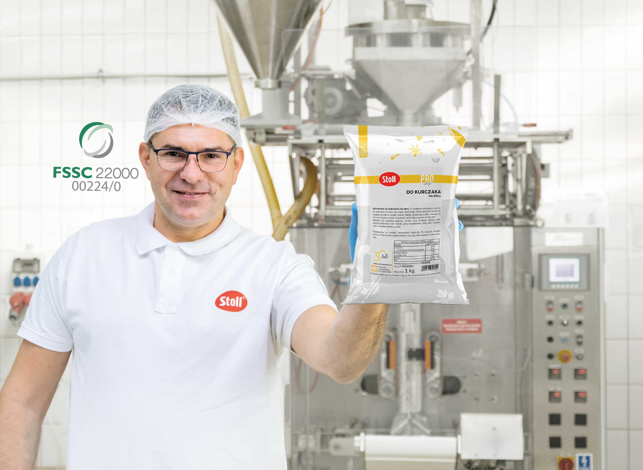 Pracownik w czepku i okularach prezentuje opakowanie przyprawy do kurczaka Stoll Pro Chef na tle linii produkcyjnej z certyfikatem FSSC 22000.