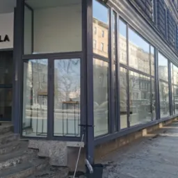 Umyta witryna sklepowa z widocznym mopem i wiadrem na chodniku, refleksy budynków w czystych szybach.