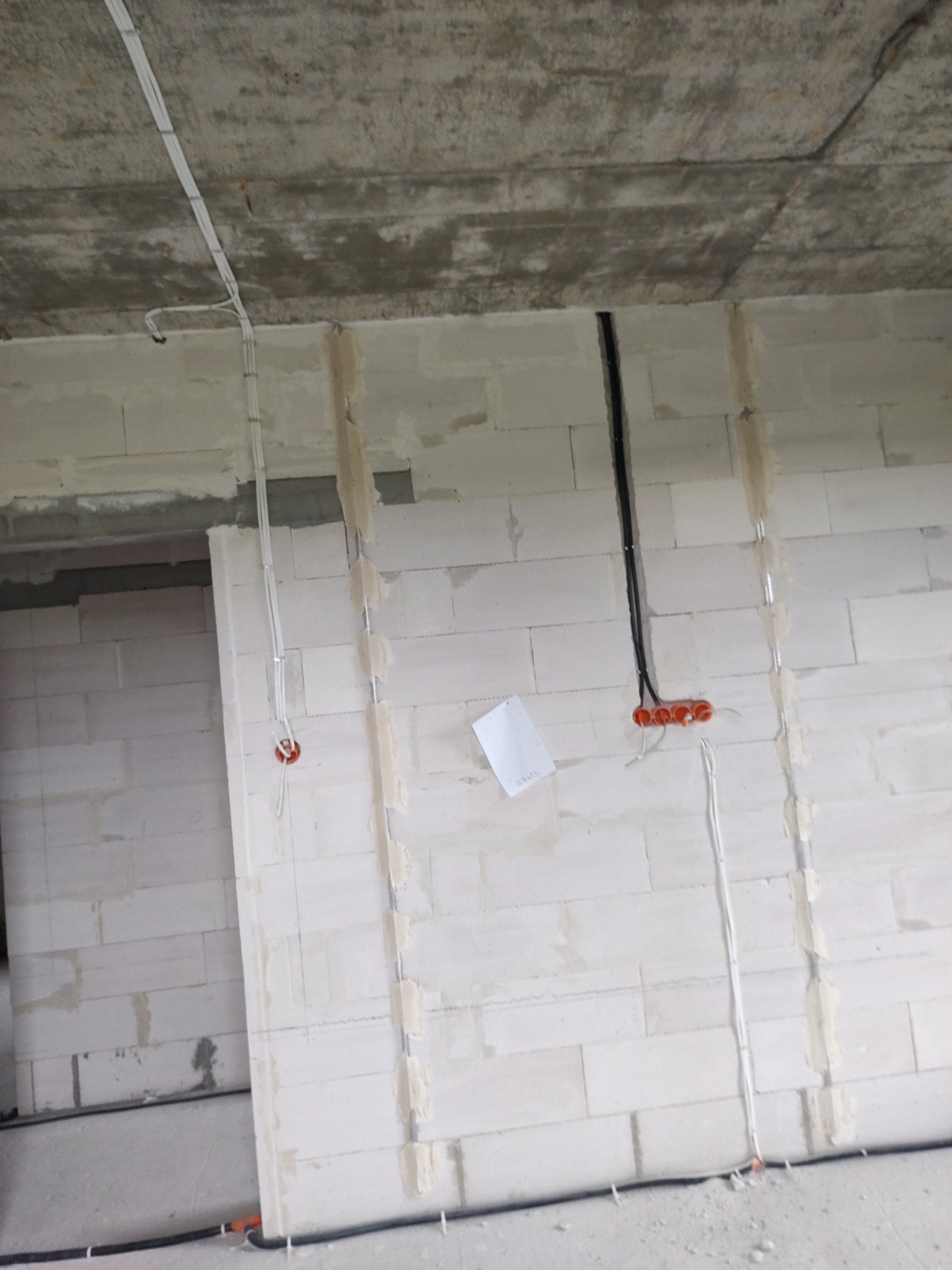 Surowy stan budynku z widocznymi przewodami elektrycznymi, częściowo zamaskowanymi gipsem w bruzdach ściennych, oraz puszkami instalacyjnymi w ścianie z betonu komórkowego.
