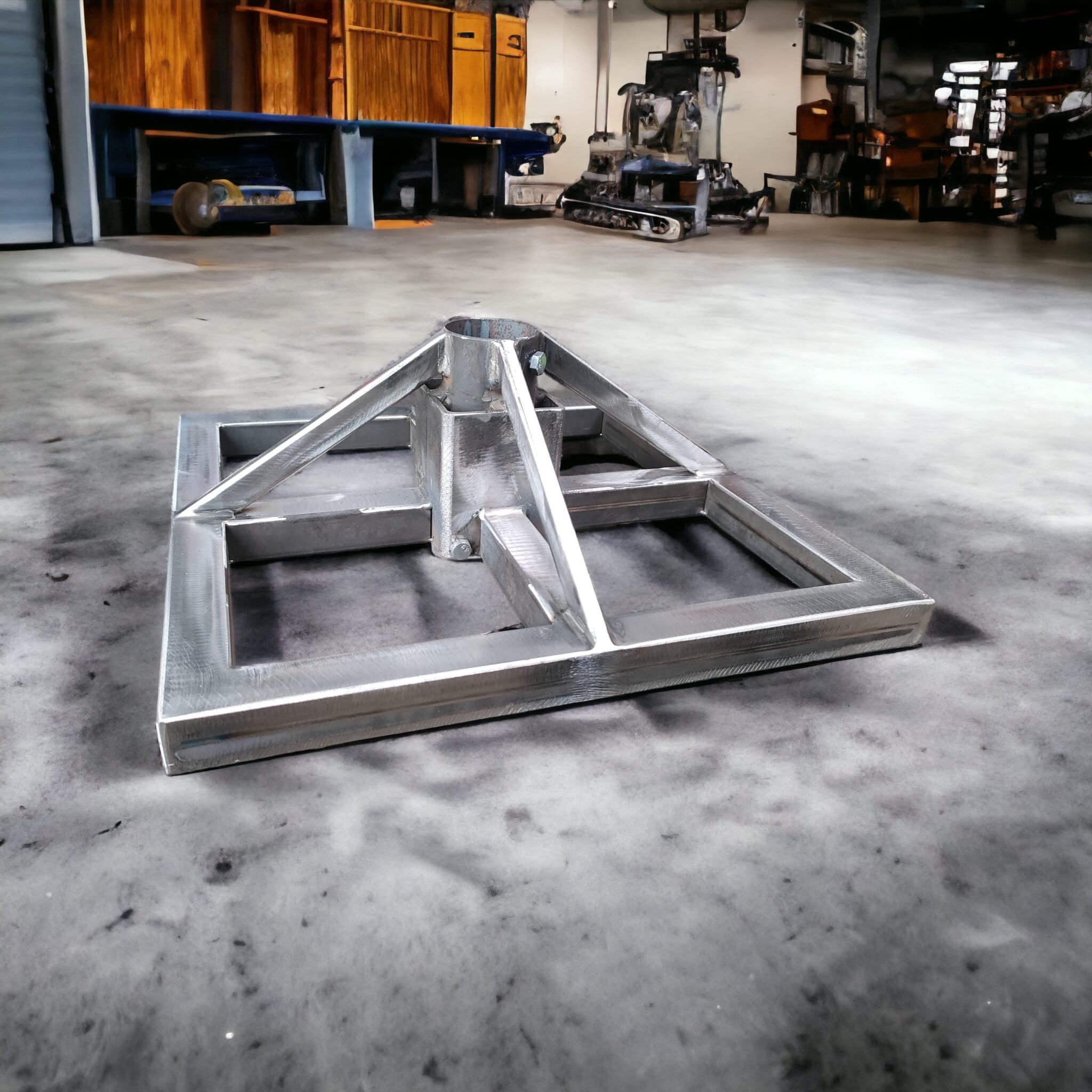 Metalowa konstrukcja nośna z profilu zamkniętego, spawana, z centralnym pionowym elementem, na betonowej posadzce hali, w tle maszyny i narzędzia.