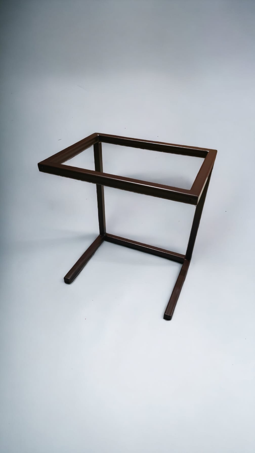 Metalowa rama stolika kawowego o kwadratowej podstawie i blacie, pomalowana na brązowo, widoczna na jasnoszarym tle.