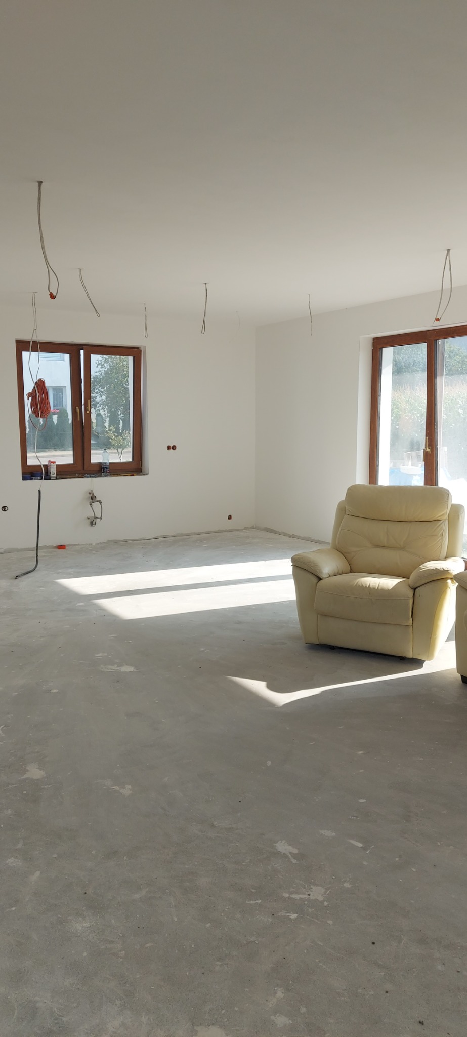 Pokój w trakcie wykańczania w Połchówku: gołe ściany, surowa wylewka podłogowa, wystające kable elektryczne i skórzany fotel w rogu, czekający na lepsze czasy.