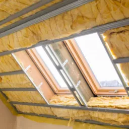 Ocieplenie poddasza wełną mineralną z widocznymi oknami dachowymi i metalową konstrukcją nośną