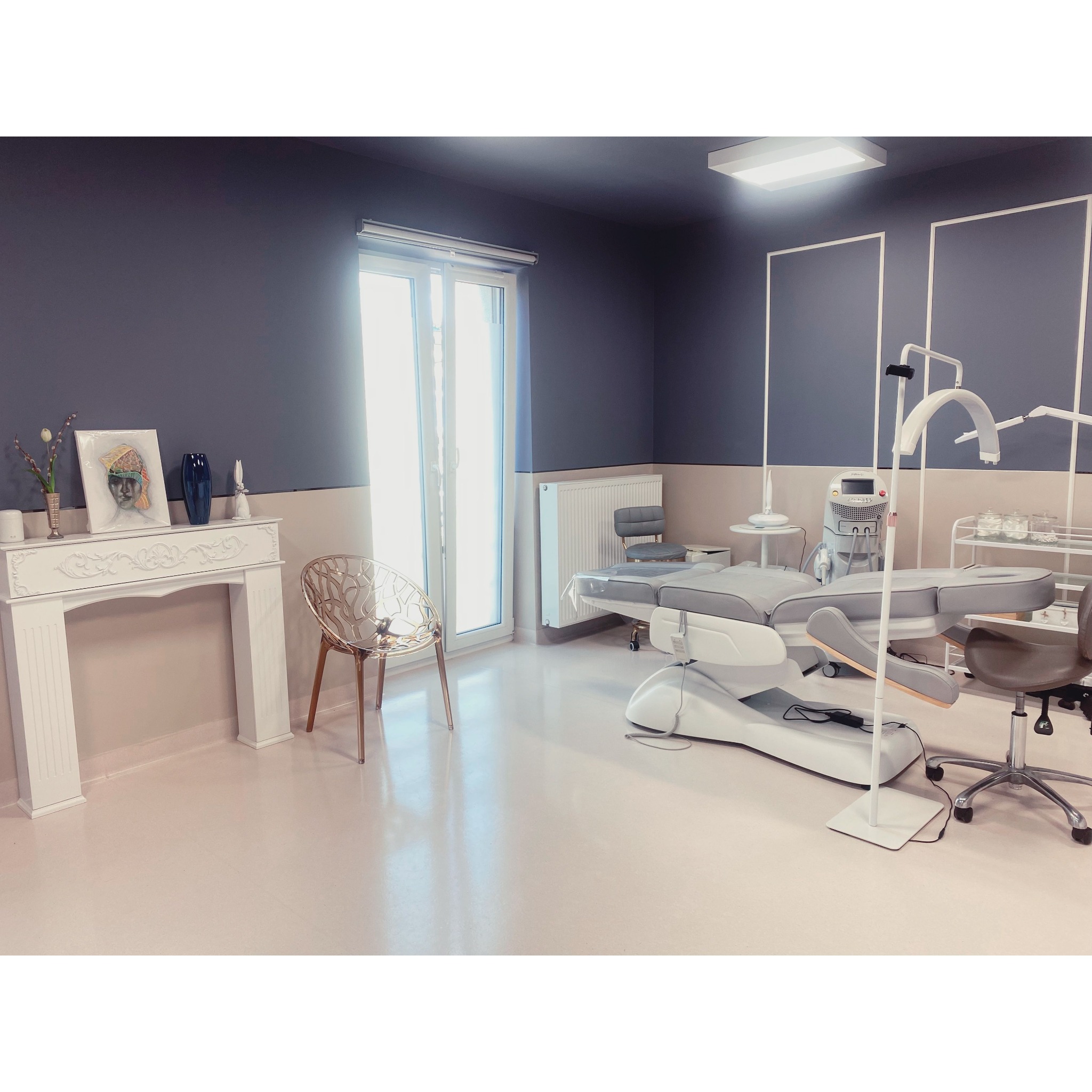 Jasne wnętrze gabinetu medycyny estetycznej z nowoczesnym fotelem zabiegowym, dekoracyjnym kominkiem z obrazem i złotym krzesłem ażurowym.