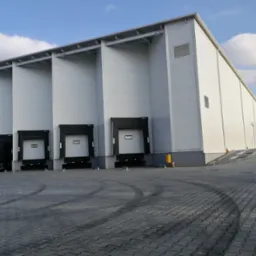 Nowoczesny budynek magazynowy z rampami załadunkowymi i zaparkowanym busem dostawczym na szarym brukowanym placu