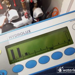 WaterLeak.pl - Osuszanie Budynków Wykrywanie Wycieków Wody Wynajem Osuszaczy Lokalizacja Przecieków Gdynia Gdańsk Sopot Warszawa - Miernik HYDROLUX firmy SebaKMT używany do pomiaru ciśnienia w instalacji hydraulicznej, widoczny ekran z wykresem słupkowym i podłączone rury z zaworami w tle.