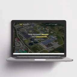 Laptop wyświetla stronę internetową firmy świadczącej usługi asenizacyjne w Warszawie, prezentującą widok z lotu ptaka na oczyszczalnię ścieków.