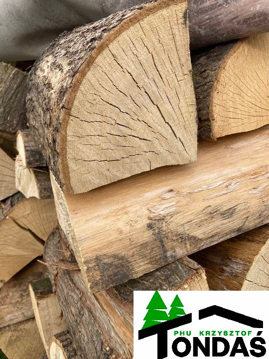Stos drewna kominkowego, z widocznym przekrojem pnia i korą. Na pierwszym planie logo firmy. Jasne drewno ułożone w stos, gotowe do użycia.