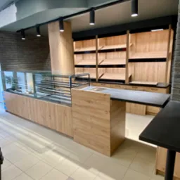 Nowoczesne wyposażenie sklepu z drewnianymi elementami: witryna chłodnicza z czarną ramą, półki ekspozycyjne i lada z blatem w kolorze antracytowym, oświetlenie punktowe na szynoprzewodzie.