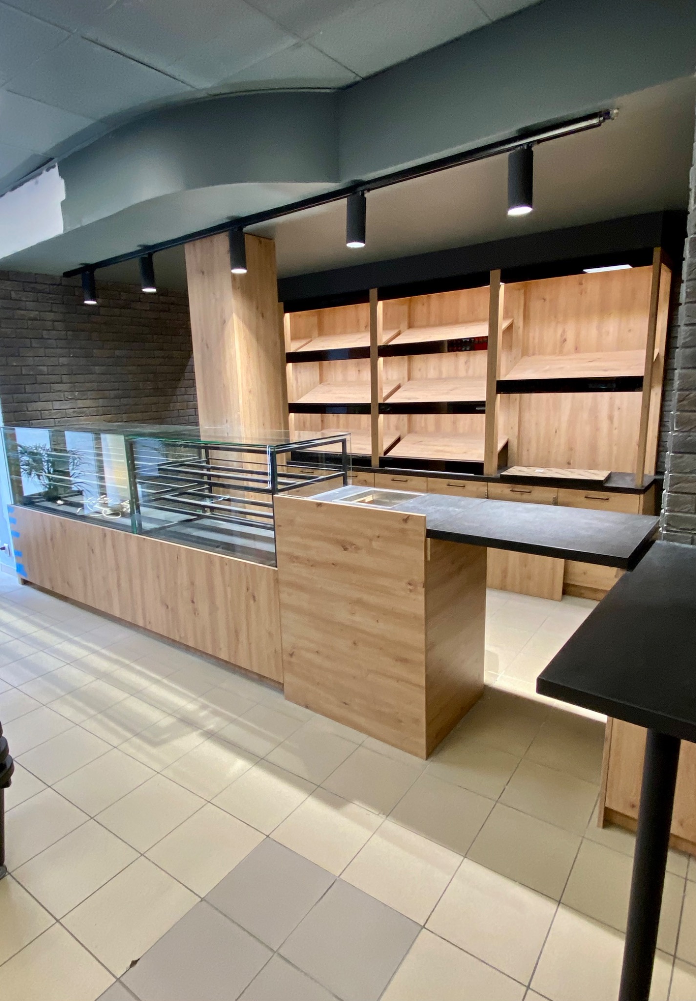 Nowoczesne wyposażenie sklepu z drewnianymi elementami: witryna chłodnicza z czarną ramą, półki ekspozycyjne i lada z blatem w kolorze antracytowym, oświetlenie punktowe na szynoprzewodzie.