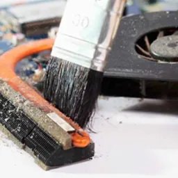 Czyszczenie zapylonego radiatora i wentylatora procesora komputera pędzlem przez osobę w rękawiczkach ochronnych, widoczna płyta główna w tle.