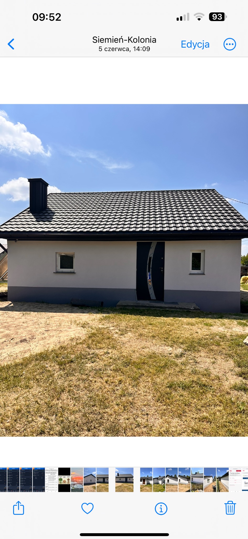 Jednopiętrowy dom z szarą elewacją, ciemnym dachem z blachy i czarnym kominem, sfotografowany w słoneczny dzień.