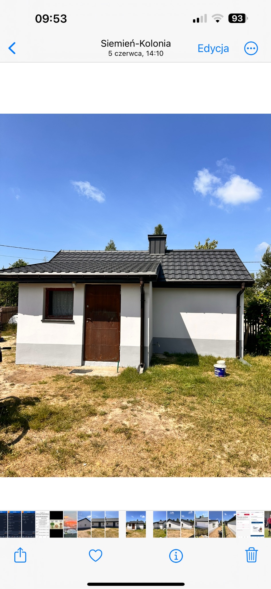 Niski budynek gospodarczy z nową, czarną dachówką i świeżo pomalowaną elewacją w kolorze biało-szarym, widoczne puszki po farbie.