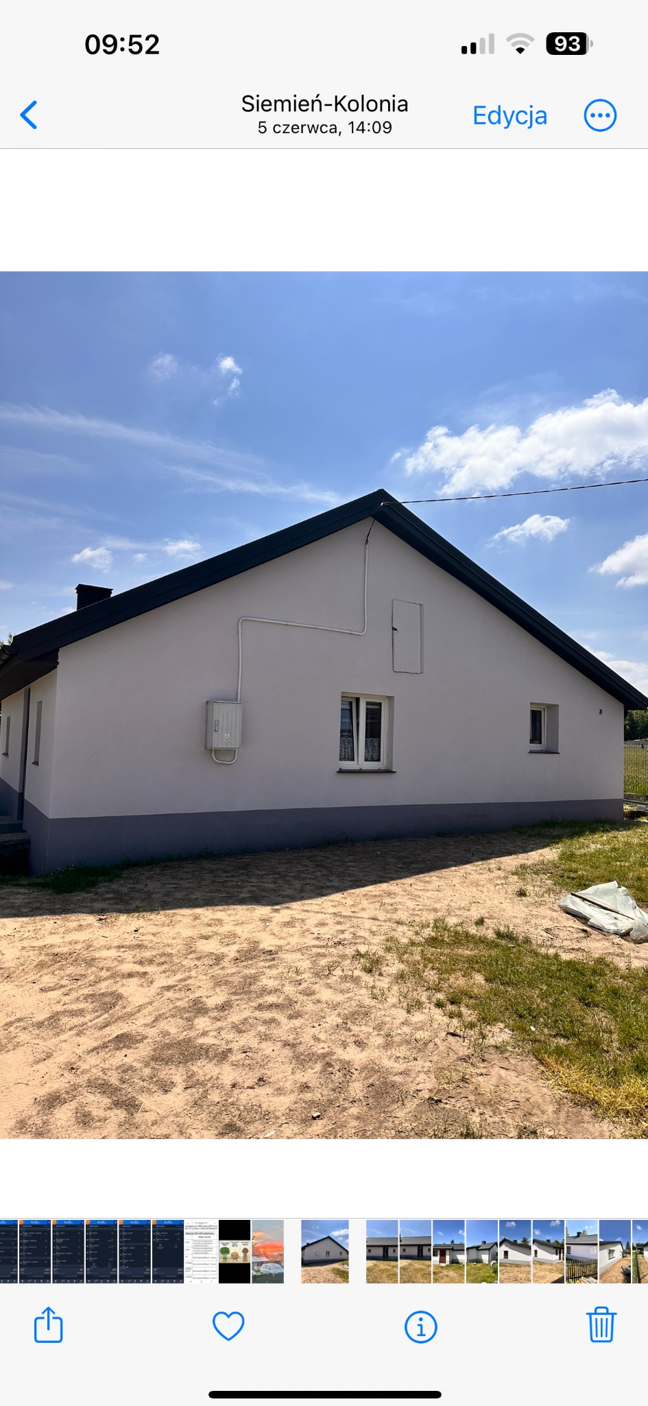 Świeżo pomalowany dom jednorodzinny z szarą podmurówką i białymi ścianami, widoczny z boku, z instalacją elektryczną na elewacji i niezagospodarowanym terenem wokół.