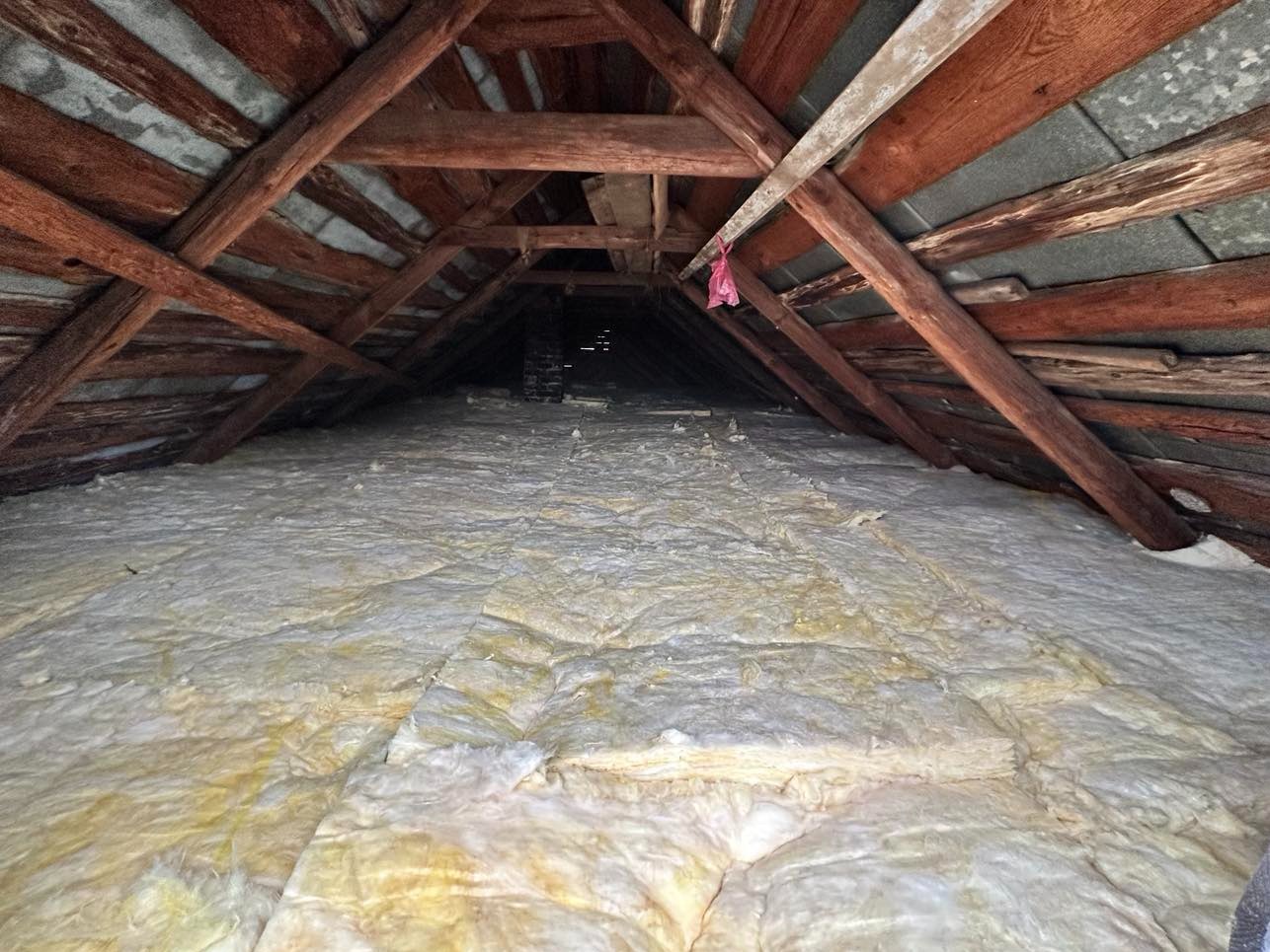 Poddasze z widoczną drewnianą konstrukcją dachu i warstwą izolacji z wełny mineralnej, widok z dołu w głąb przestrzeni.