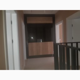 Ekodom - Korytarz z zabudową meblową pod telewizor, widoczne kable wystające ze ściany, elementy wykończeniowe w trakcie montażu.