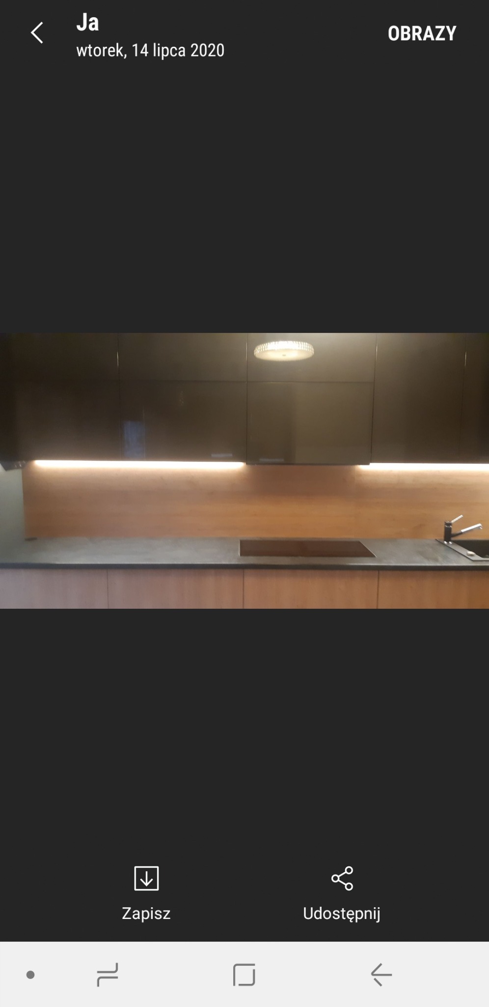 Nowoczesna kuchnia z ciemnymi, lakierowanymi szafkami górnymi i drewnopodobnymi szafkami dolnymi, podświetleniem LED pod szafkami górnymi i okrągłą lampą sufitową.