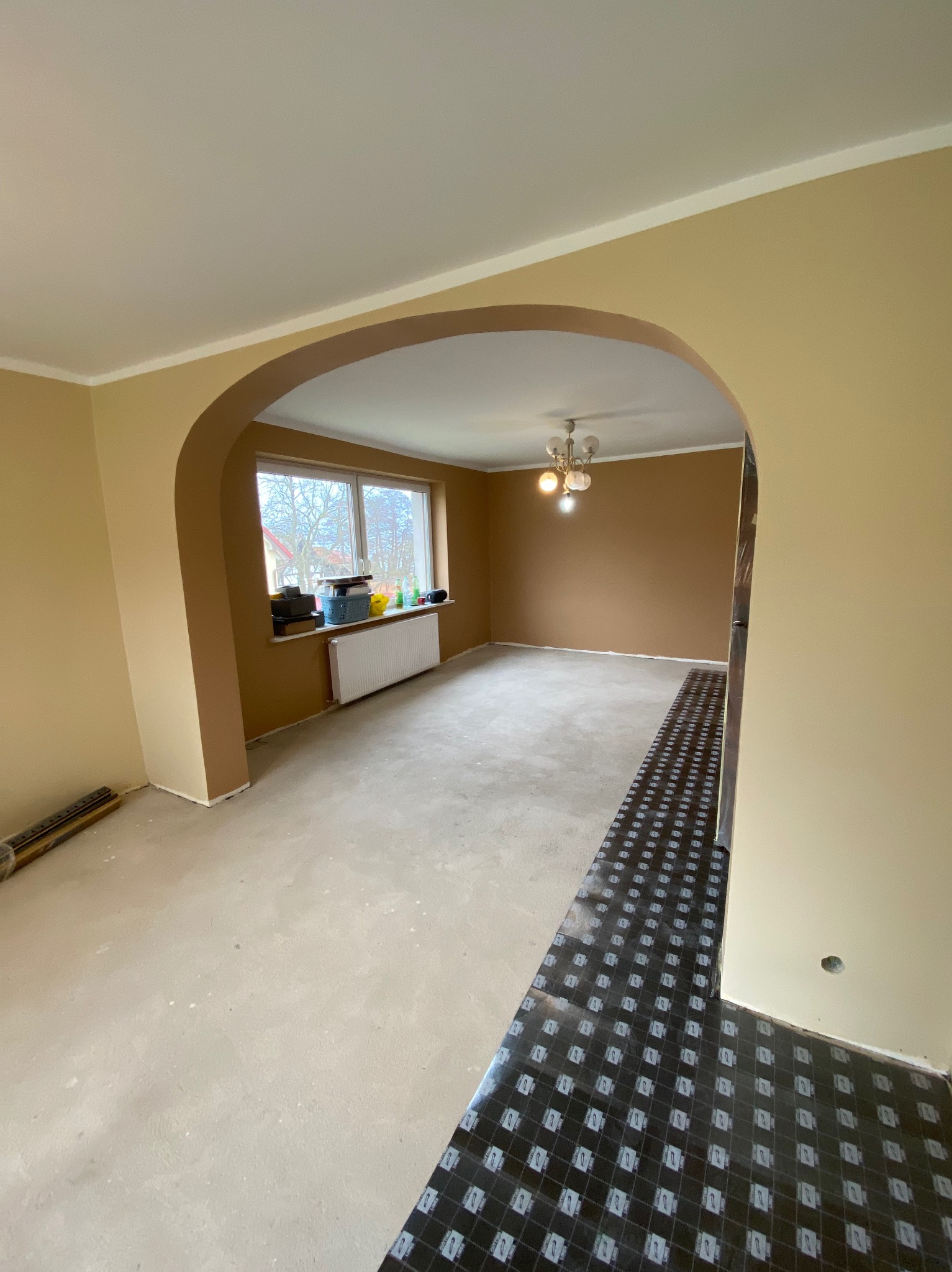 Przygotowanie do układania podłogi w pokoju z łukowym przejściem, widoczne panele podkładowe, świeżo pomalowane ściany w odcieniach beżu i brązu, surowa wylewka podłogowa.