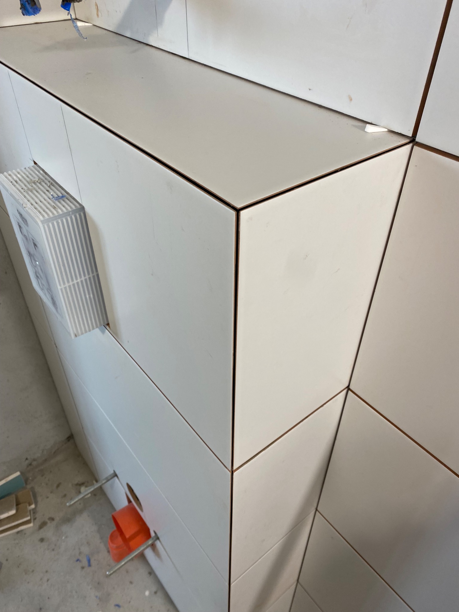 Białe płytki ułożone pod kątem na ścianie w łazience, widoczne elementy instalacji hydraulicznej i stelaż podtynkowy.