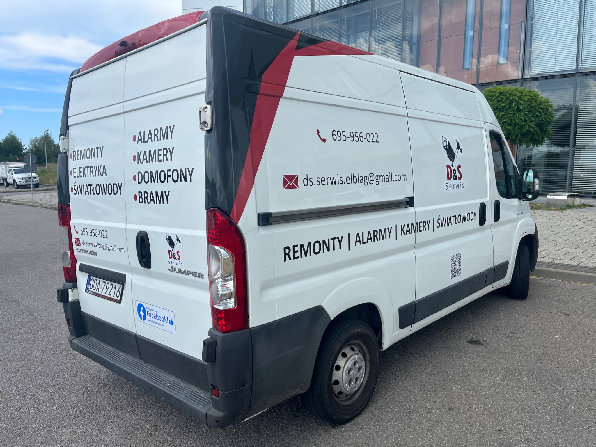 Biały samochód dostawczy firmy serwisowej z Elbląga, z widocznymi numerami telefonów, adresem e-mail, logiem firmy i wypisanymi usługami: remonty, elektryka, alarmy, kamery, domofony, bramy...