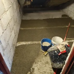 Niedokończone ocieplenie poddasza z widoczną warstwą izolacji, pustakami i narzędziami budowlanymi w trakcie realizacji.