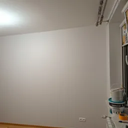 Świeżo pomalowana ściana w pokoju, widoczne puszki z farbą Dekoral Łazienka & Kuchnia na parapecie, gniazdko elektryczne przy podłodze.